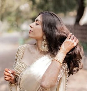 Simran in an ivory satin saree with a pearl and gold blouse, touching her hair