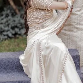 The saree's drape and pearl edging, seated on stone steps